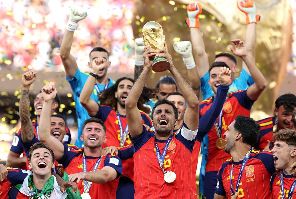 Rodri lifts the FIFA World Cup Winner’s Trophy, Spain squad celebrate behind him.